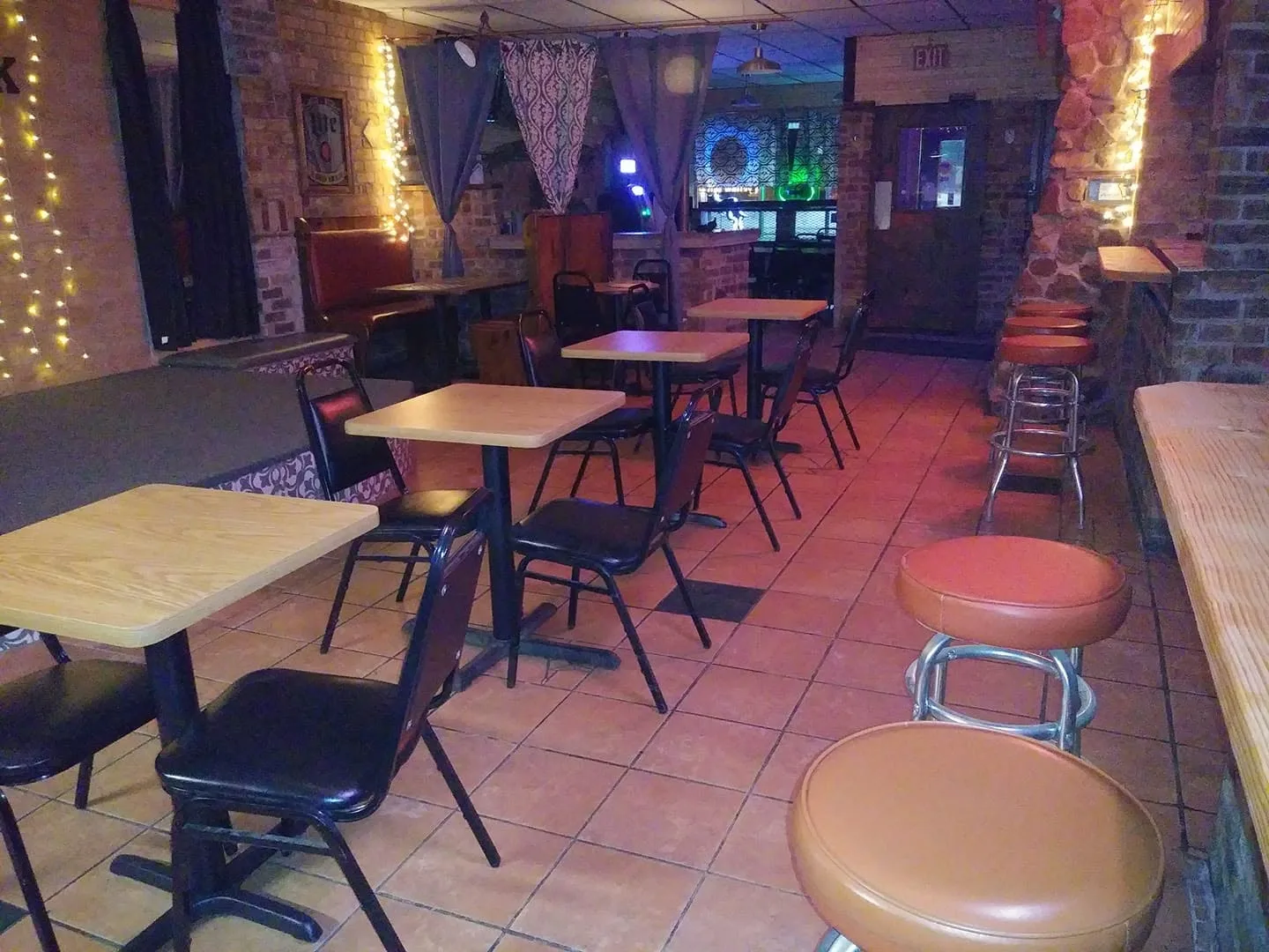 Tables and booths in the back room, brick walls and string lights, bar stools along the counter