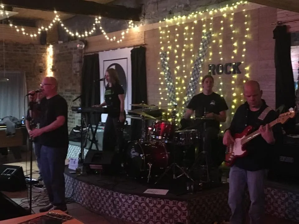 A four-piece band playing on the stage in front of a lit ROCK sign